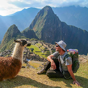 A tourist sitting with a llama with Machu Picchu in the background.